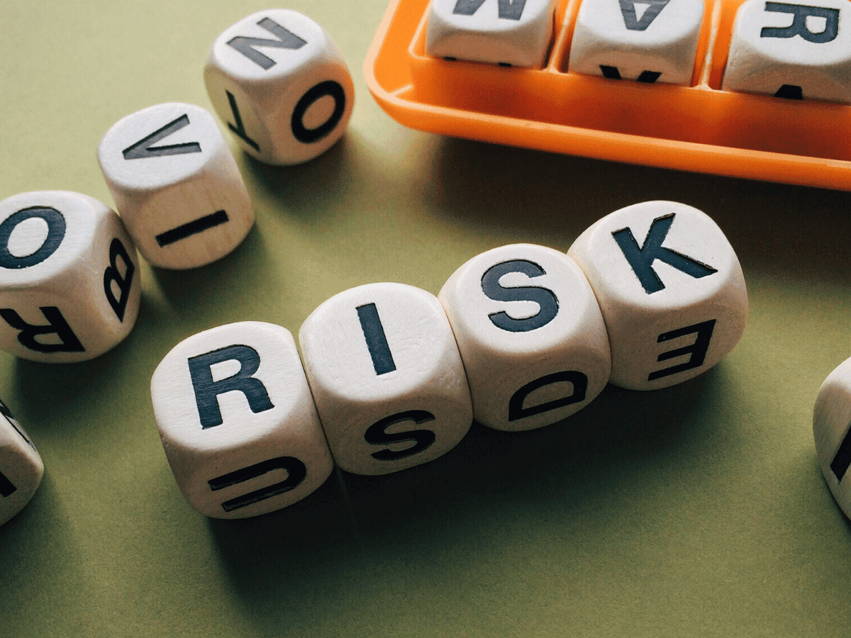 Wooden dice spell out the word "RISK" on a green surface, evoking a sense of cautious thrill, while more dice rest in an orange tray nearby, offering comfort in their orderly presence beside the chaos.