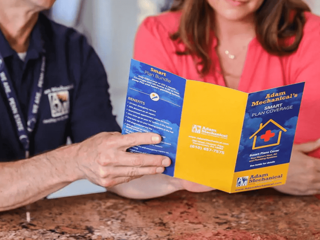 Two people are sitting at a table, reading an Adam Home Services brochure about smart plan coverage. They're intrigued by the option to replace the heater system, imagining a cozy home equipped with cutting-edge technology for comfortable living.