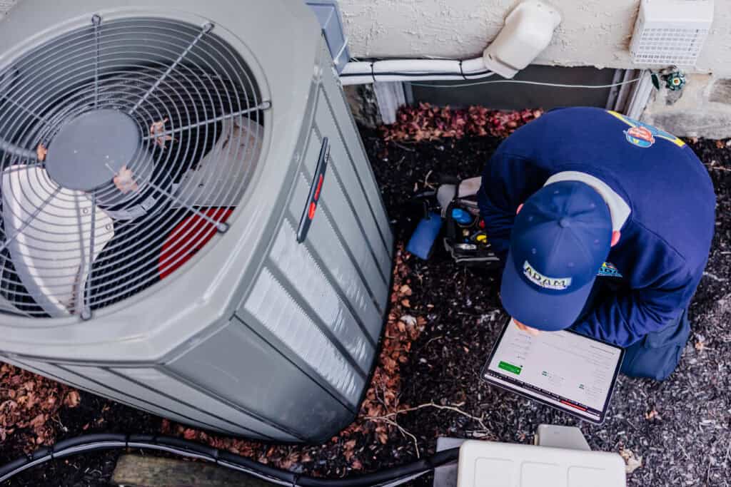 An Adam Home Services technician using a tablet checklist during a routine central air conditioning maintenance service.